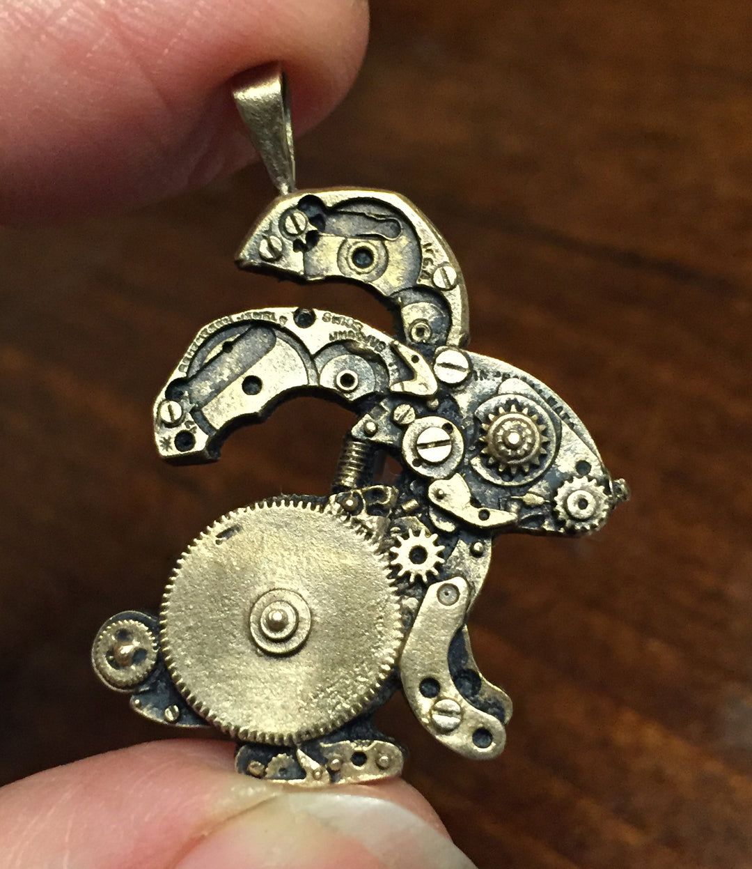 Sue Beatrice's small watch parts bunny pendant in bronze held between 2 fingers.