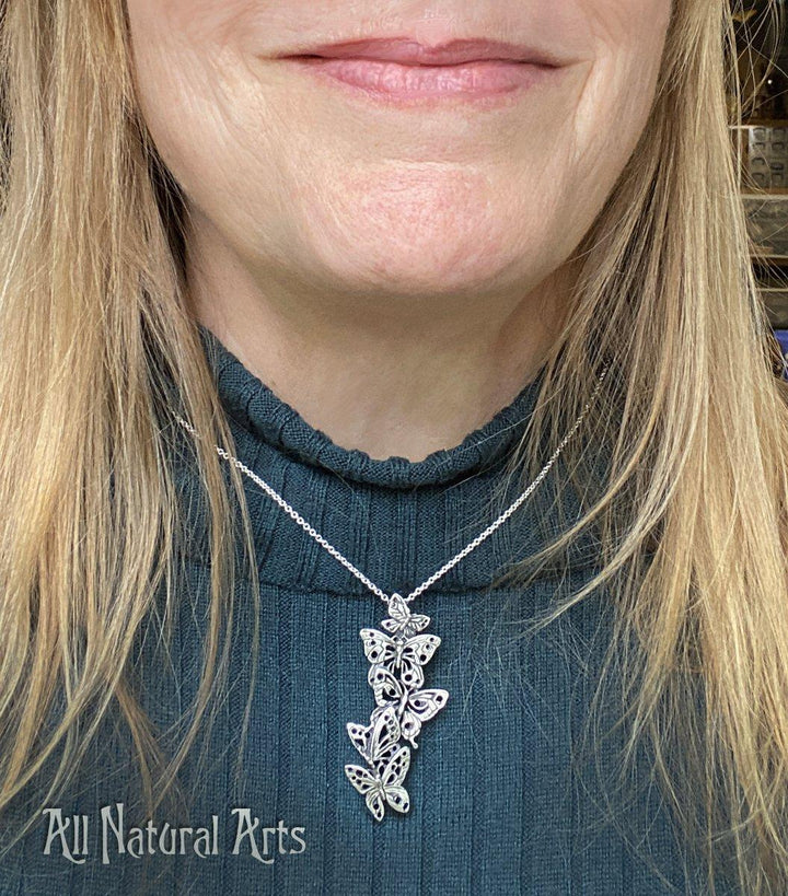 A young woman wearing the Ascending Butterflies Necklace by Sue Beatrice of All Natural Arts. The necklace features a filigree design with five ascending butterflies crafted from solid sterling silver, suspended from an 18-inch sterling silver chain. 