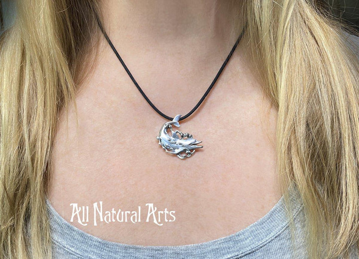 A girl wearing a sterling, silver dolphin, happily swimming with bubbles coming off his body on a black silicone cord.