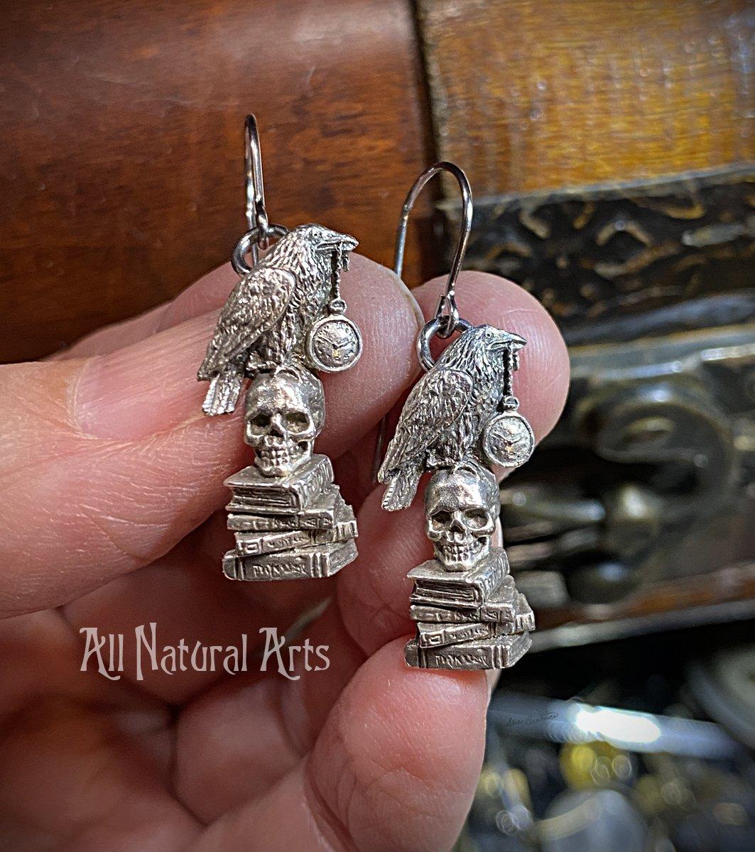 Earrings with raven grasping a pocket watch in its beak, perched atop a skull resting on a stack of books