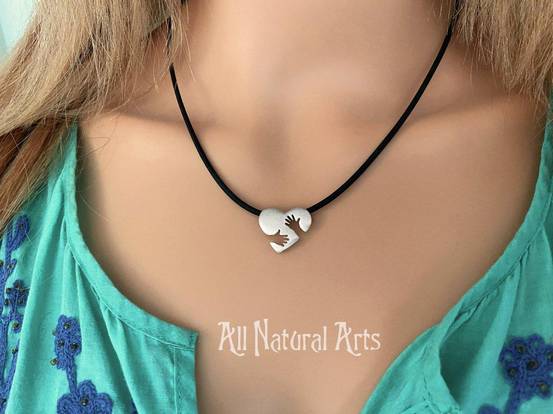 Close-up of the sterling silver Everlasting Hug pendant on a black cord on a model.