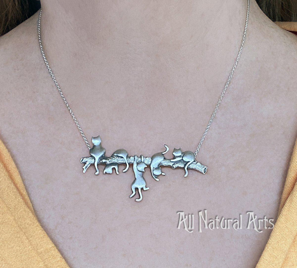 A girl wearing an endearing silver necklace with 5 playful cats on a branch. Adorable!