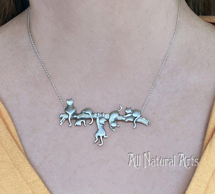 A girl wearing an endearing silver necklace with 5 playful cats on a branch. Adorable!