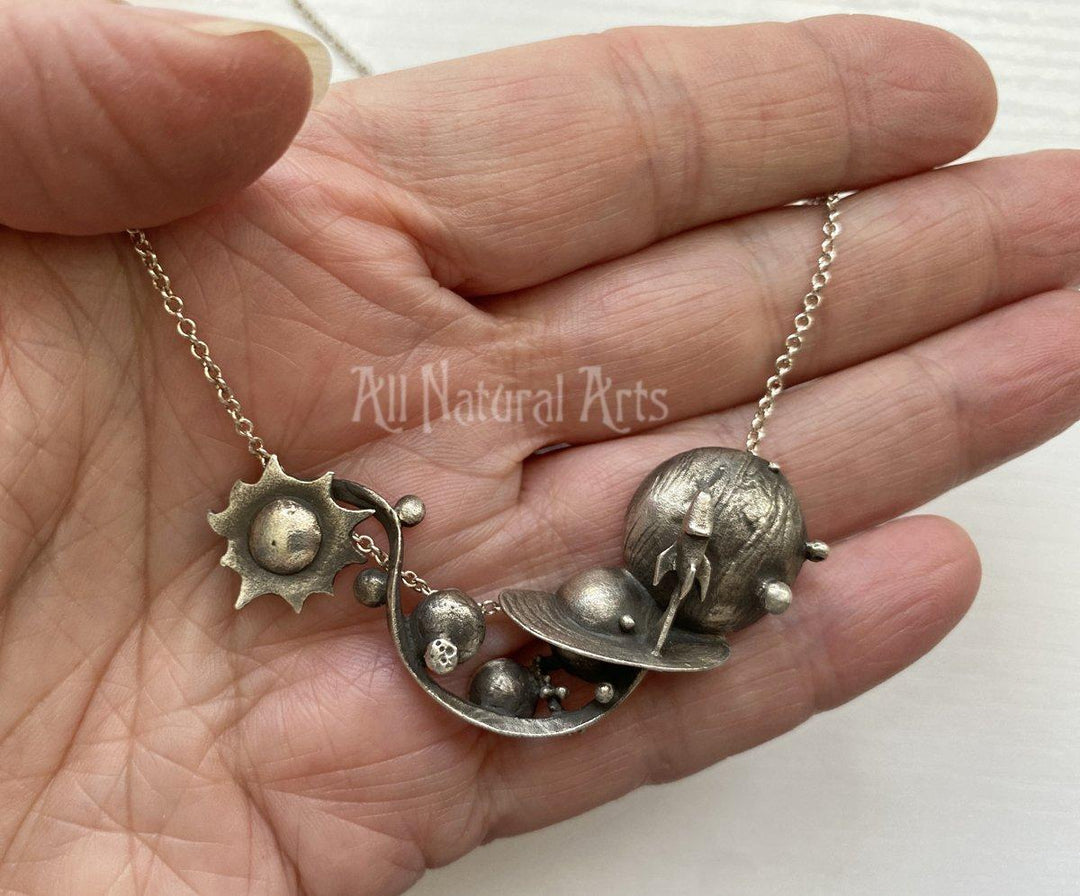 Silver Planets necklace On silver chain held in hand.