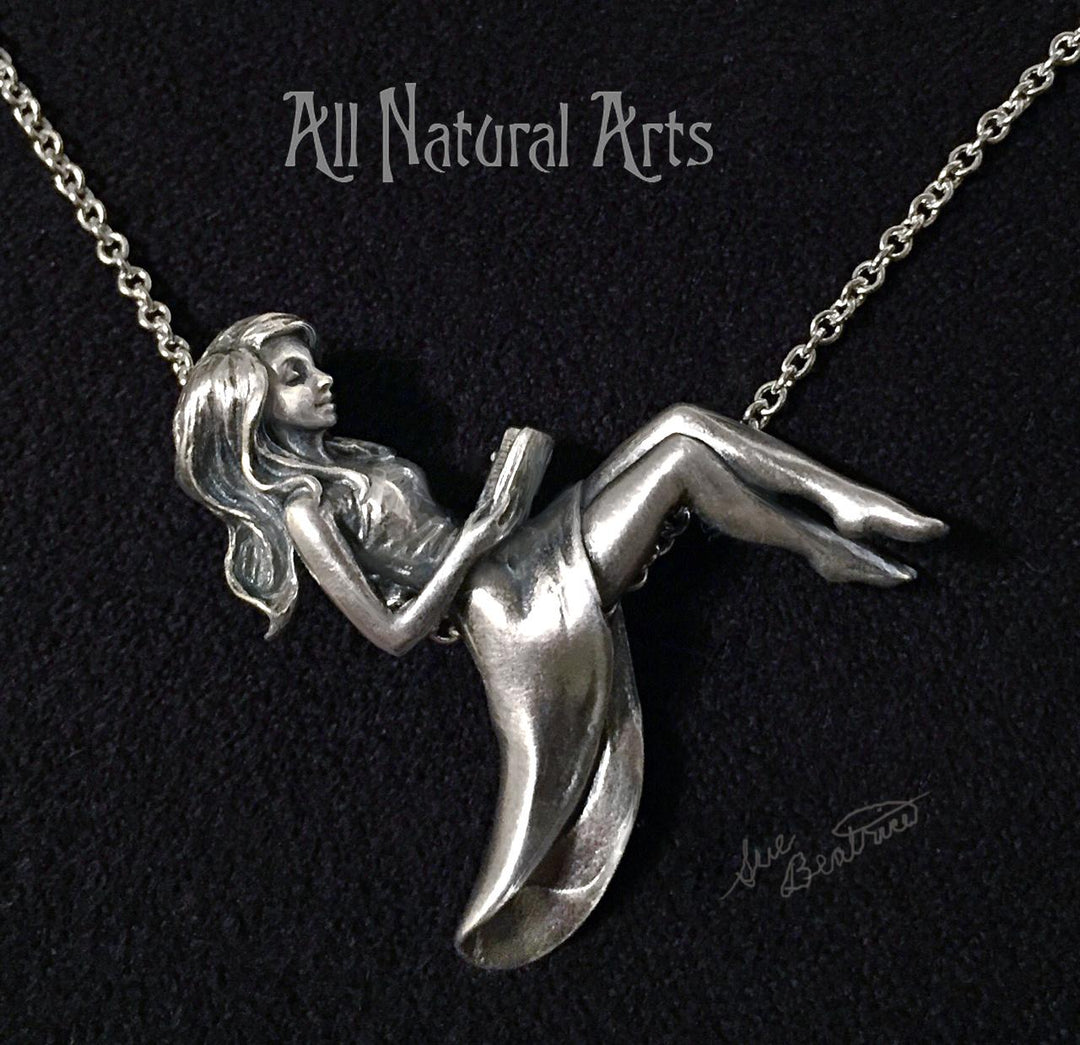 Silver pendant of girl reclining on chain reading a book.