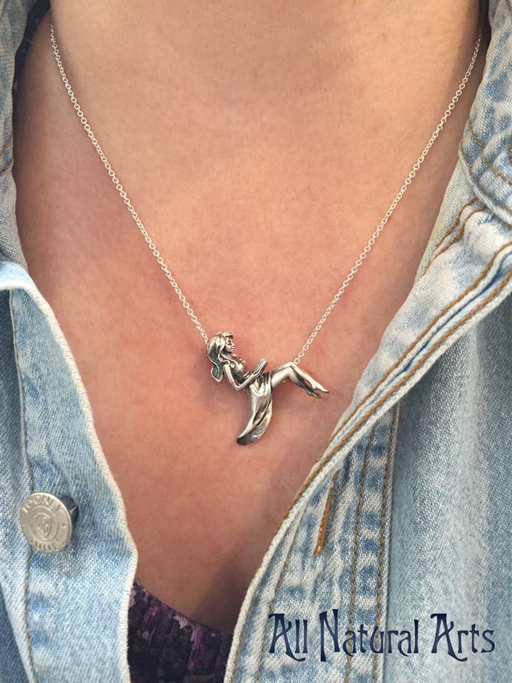 Girl wearing a silver pendant of girl reclining on silver chain reading a book.