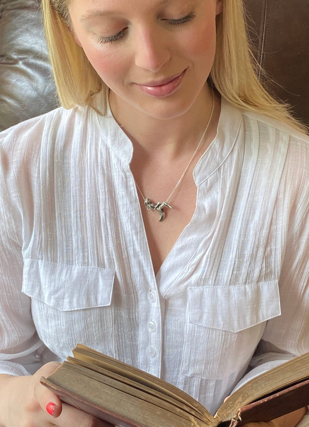 Girl reading a book wearing a silver pendant of girl reclining on silver chain reading a book.
