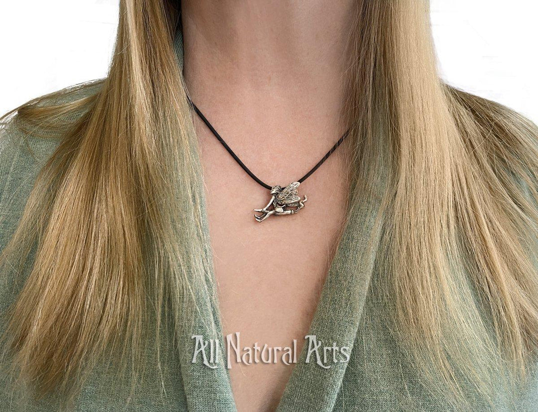 Woman wearing a pendant of Silver weed fairy riding a joint with smoke rising from the back.