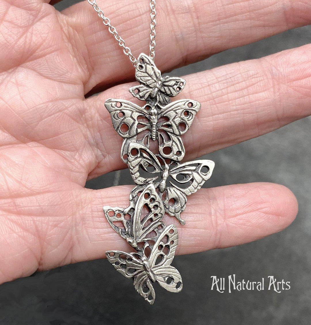 A close up photo of a person holding Ascending Butterflies Necklace by Sue Beatrice of All Natural Arts. Solid sterling silver filigree design with 5 ascending butterflies on an 18-inch chain.