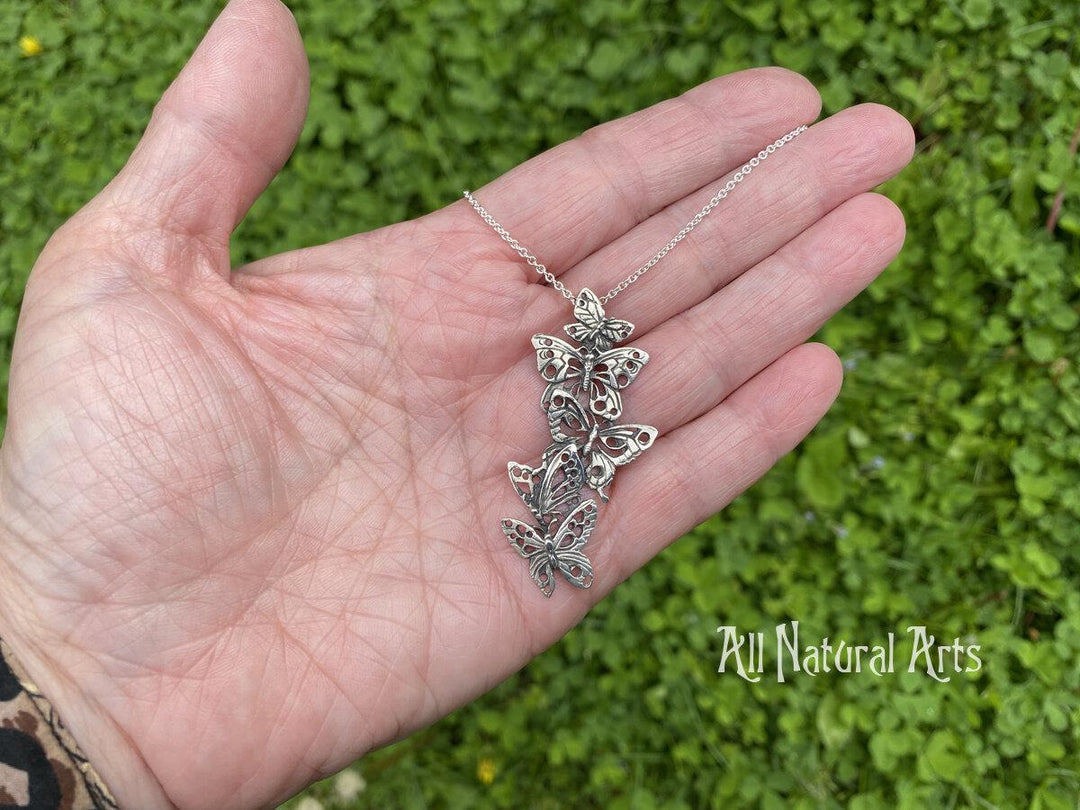 A person holding Ascending Butterflies Necklace by Sue Beatrice of All Natural Arts. Solid sterling silver filigree design with 5 ascending butterflies on an 18-inch chain.