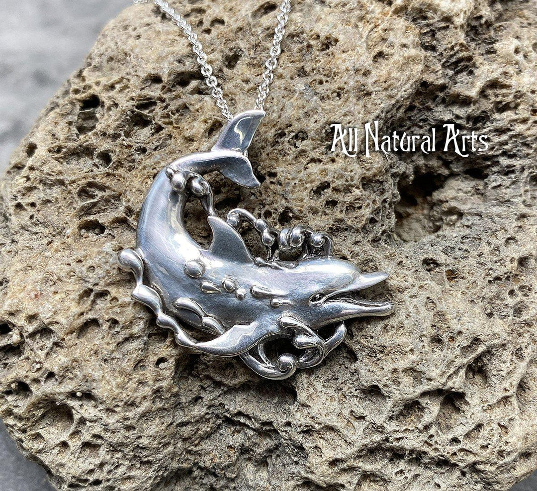 a sterling, silver dolphin, happily swimming with bubbles coming off his body on a sterling silver chain resting on a coral background