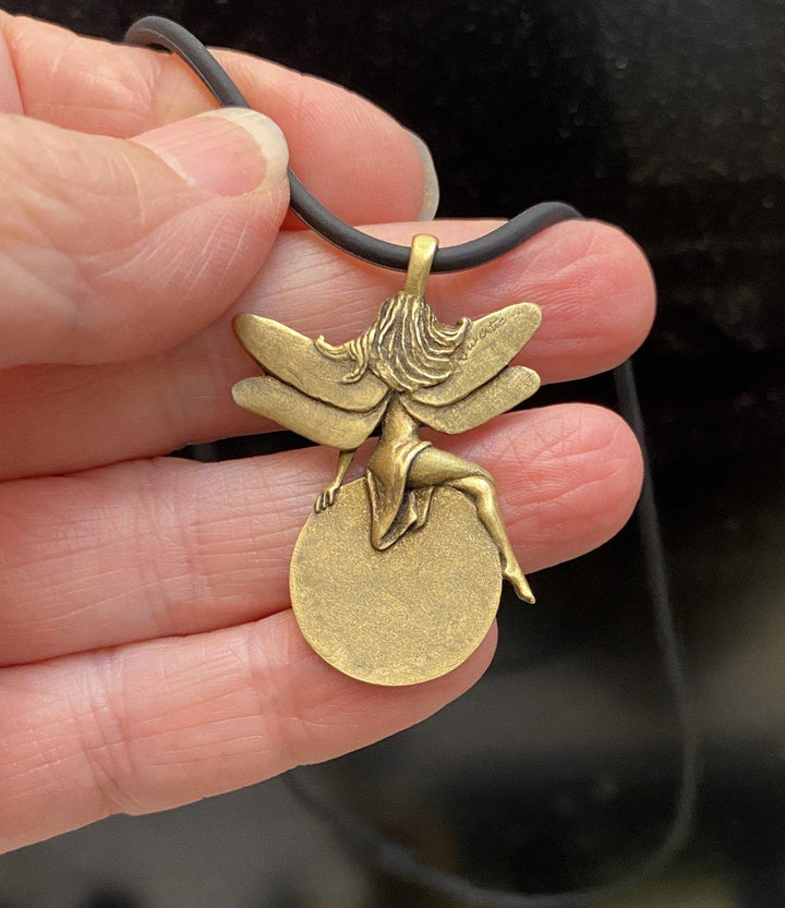 In hand: fully carved back of Lucky Lady Lottery Fairy - Gold-toned brass charm with four-leaf clovers, perfect for lottery luck. On a black silicone cord.