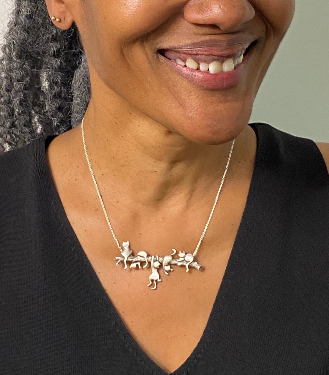 A woman wearing an endearing silver necklace with 5 playful cats on a branch. Adorable!