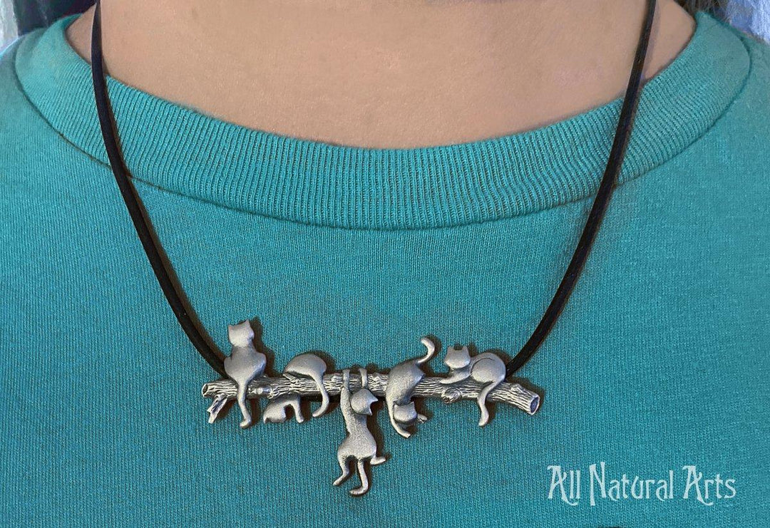 A girl wearing an endearing silver necklace with 5 playful cats on a branch. Adorable!