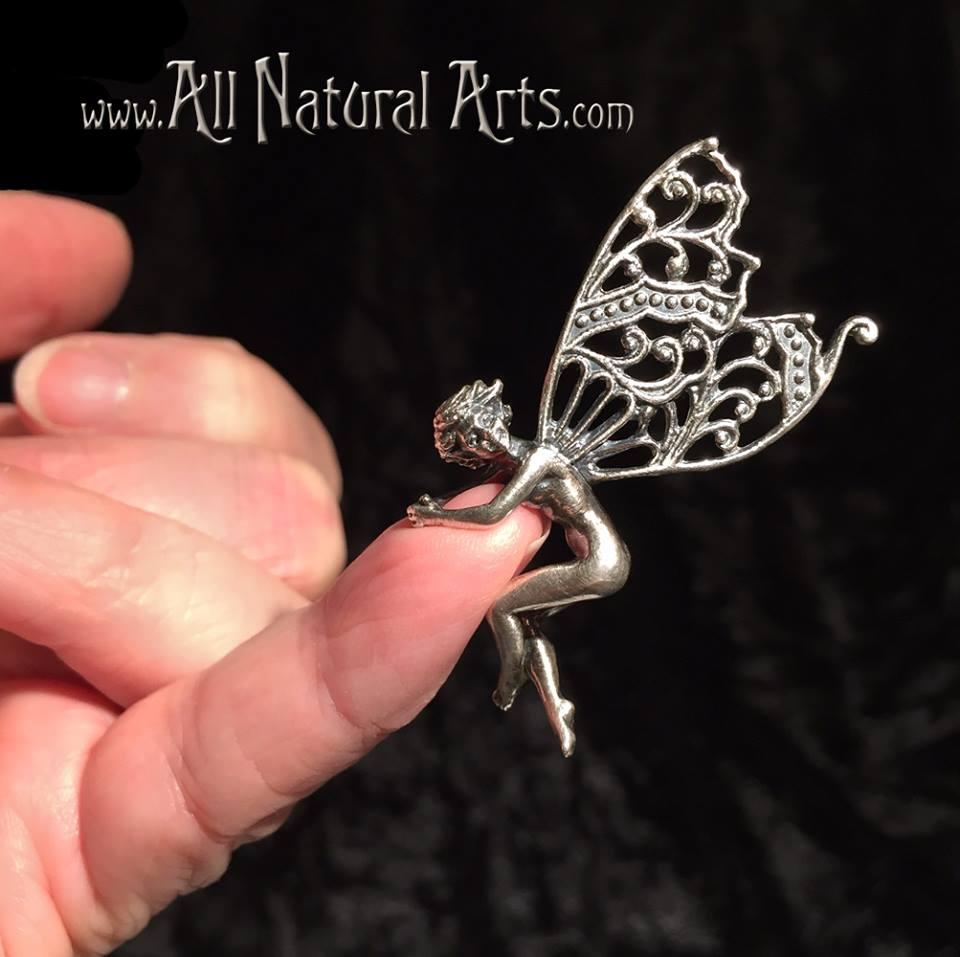 Silver sprite pendant playfully hangs onto a finger. 