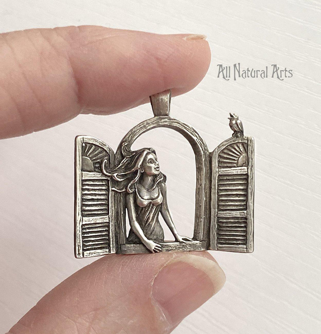 Girl in the Window Necklace: Sterling silver pendant held delicately between two fingers.