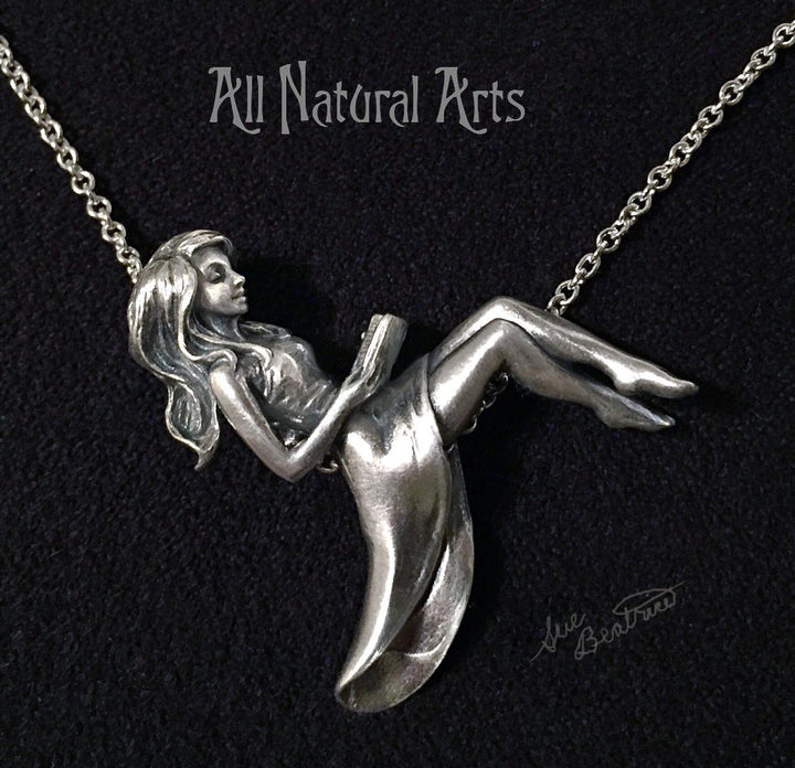 Silver pendant of girl reclining on chain reading a book. 